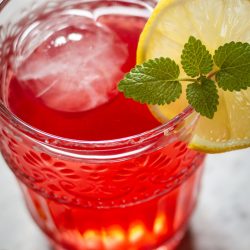 Fruchtiger Cranberry-Eistee: Unser liebstes Rezept für heiße Tage Eisgekühlter Cranberry-Eistee in einem Glas mit frischer Minze und Zitronenscheiben an einem sonnigen Tag.
