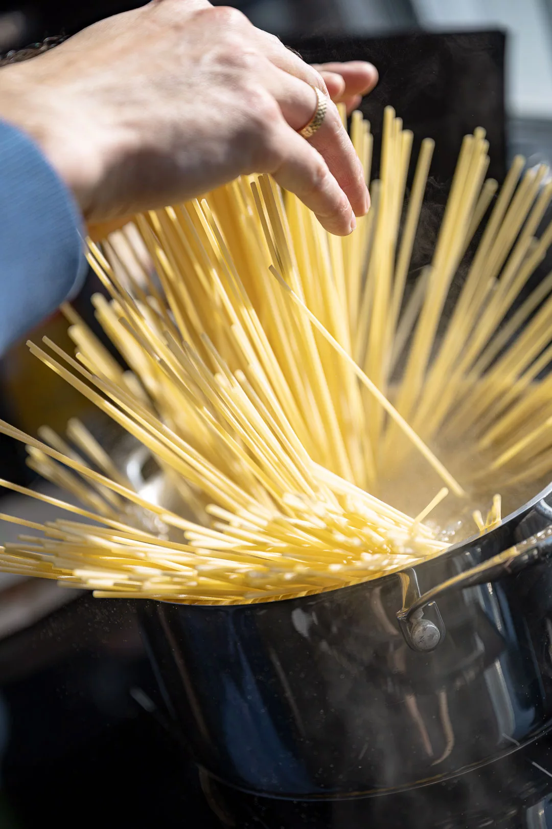 Hände geben trockene Spaghetti in einen großen Topf mit kochendem Wasser.