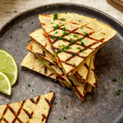 Goldbraun geröstete Quesadilla-Hälften mit geschmolzener Käsefüllung, auf einem Teller angerichtet, daneben eine Schale mit Dip.