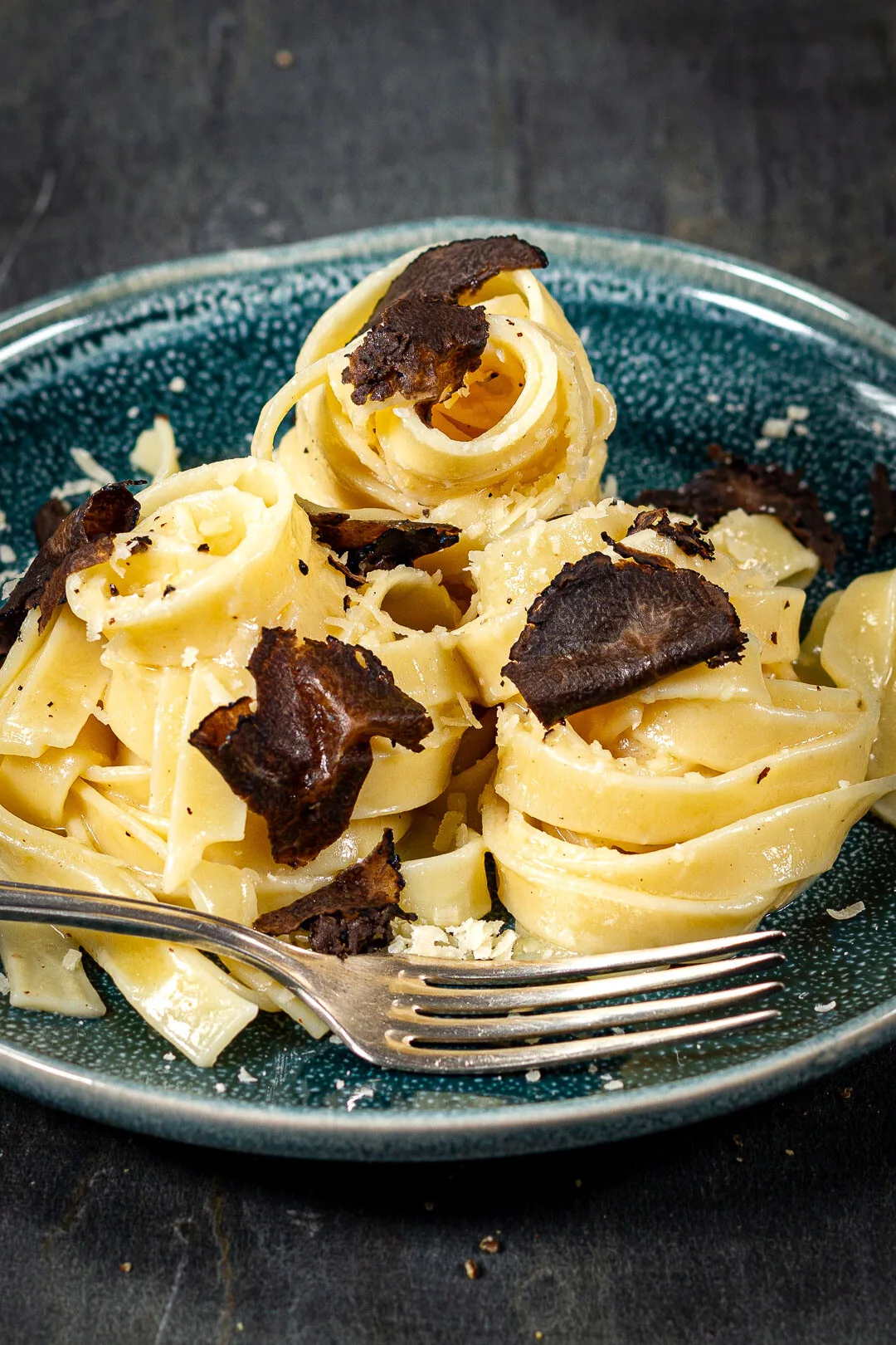 Cremige Trüffelpasta mit Tagliatelle, Parmesan und schwarzen Trüffelscheiben auf einem Teller angerichtet.