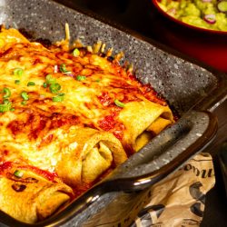 Vegetarische mexikanische Enchiladas mit frischer Tomatensalsa Frisch gebackene vegetarische Enchiladas in einer Auflaufform, mit geschmolzenem Käse und einer roten Sauce überbacken, garniert mit frischen Kräutern.