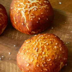 Laugen Burger Buns: Fluffiges Brioche Rezept Goldbraun gebackene Laugen Burger Buns mit grobem Salz auf einem rustikalen Holzbrett.