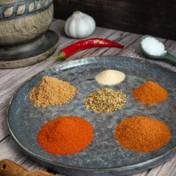 Yummy Mexico! Mexikanische Gewürzmischung in 5 Minuten selber machen – Authentisch und ohne Zusätze Verschiedene gemahlene mexikanische Gewürze wie Paprika, Kreuzkümmel und Chili, die dekorativ in kleinen Häufchen und in einem Glasgefäß auf einem dunklen Untergrund angeordnet sind.