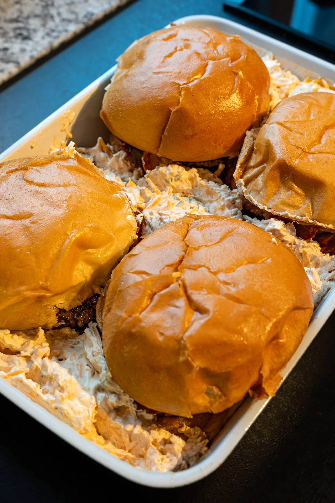 Vorbereitete Zutaten für den Auflauf vor dem Backen: Angebratener Hackfleisch-Patty, Bacon-Scheiben und leckere Käsemischung, angerichtet in einer Backform.