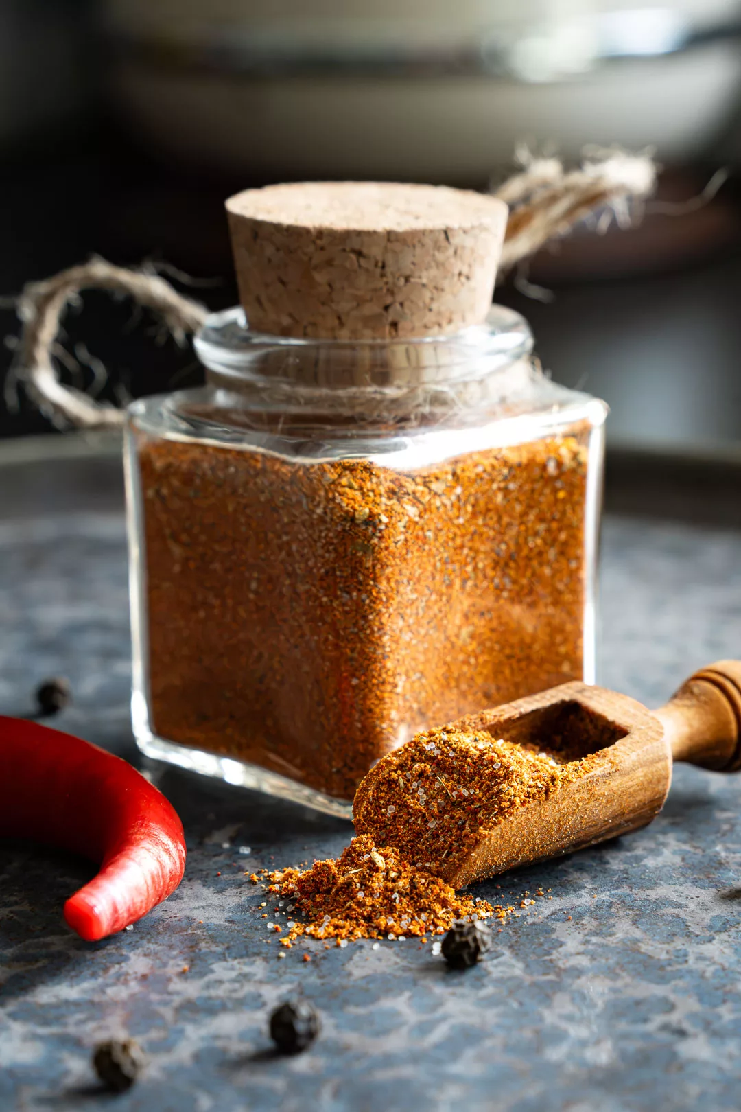 Mexikanische Gewürzmischung selber machen: Mexikanische Gewürzmischung in einer Schale, umgeben von ganzen Chilis und Pfefferkörnern auf Stein.