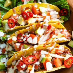 Drei fertig angerichtete mexikanische Tacos mit gebratenen Portobello-Pilzen, Limetten-Mayonnaise, frischem Koriander und Limettenspalten auf einer dunklen Platte.
