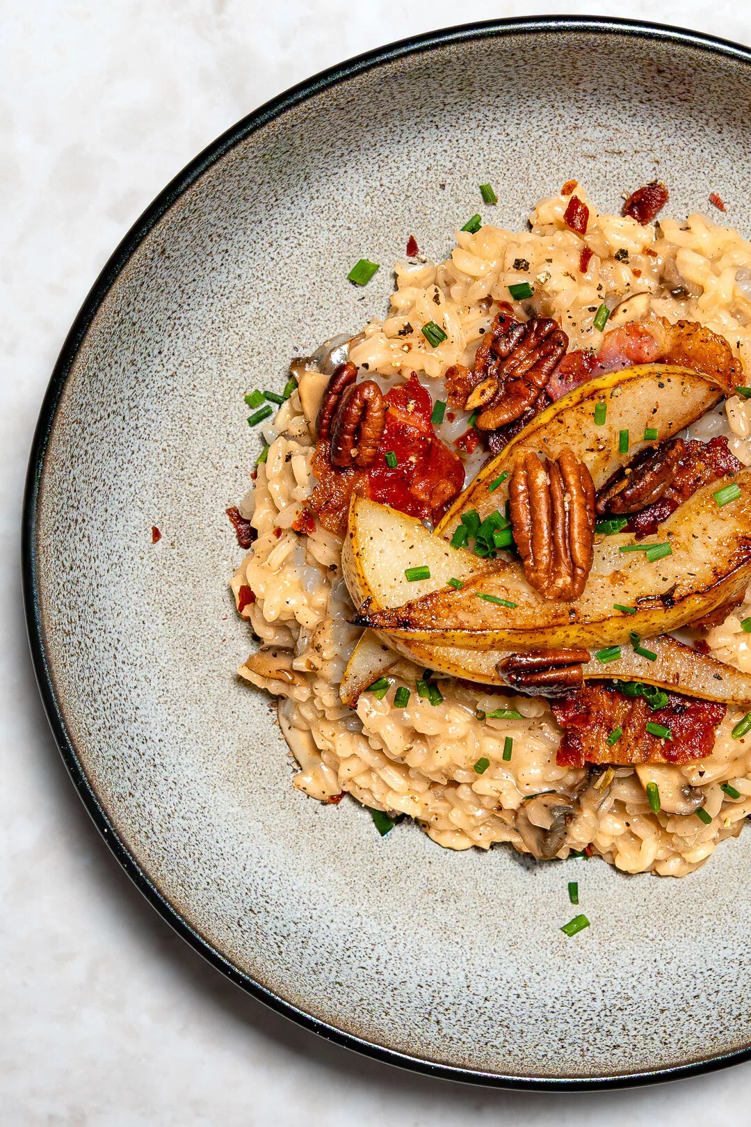 Cremiges Pilzrisotto mit Bacon, gebratenen Pilzen, Parmesan und Petersilie in weißem tiefen Teller auf dunklem Hintergrund.