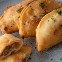 Goldbraun frittierte Tschebureki mit knusprigem Teig und saftiger Fleischfüllung, serviert auf einem Teller als herzhaftes Streetfood Gericht