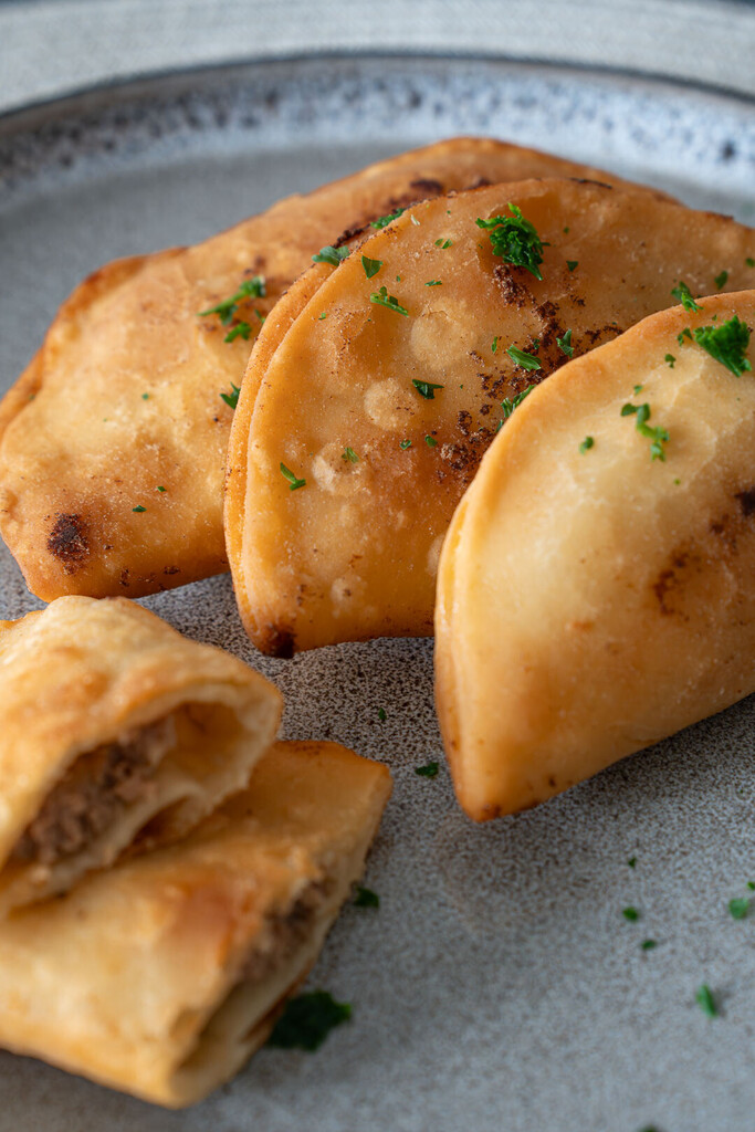 Goldbraun frittierte Tschebureki mit knusprigem Teig und saftiger Fleischfüllung, serviert auf einem Teller als herzhaftes Streetfood Gericht