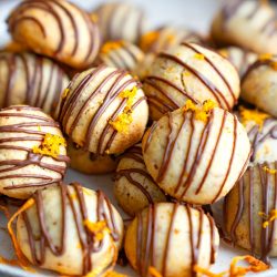 Hausgemachte Orangen-Schoko-Kekse mit Zartbitterschokoladen-Glasur und frischem Orangenabrieb auf einem hellen Teller.