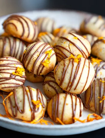 Hausgemachte Orangen-Schoko-Kekse mit Zartbitterschokoladen-Glasur und frischem Orangenabrieb auf einem hellen Teller.