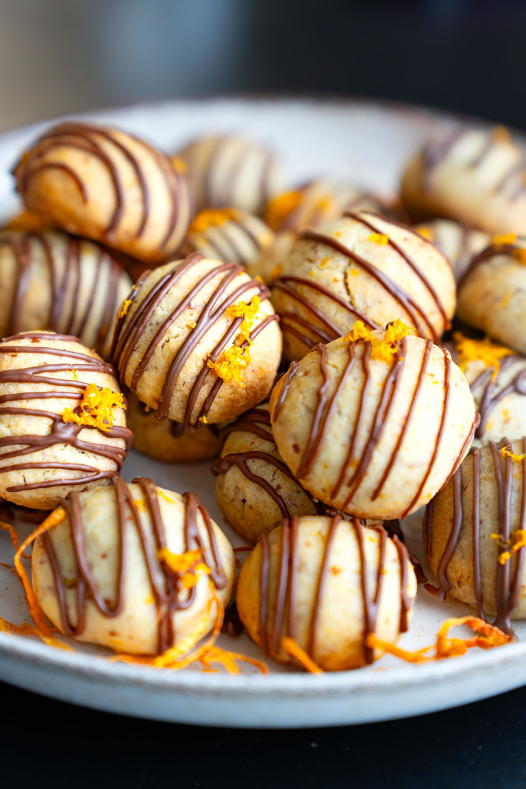 Hausgemachte Orangen-Schoko-Kekse mit Zartbitterschokoladen-Glasur und frischem Orangenabrieb auf einem hellen Teller.