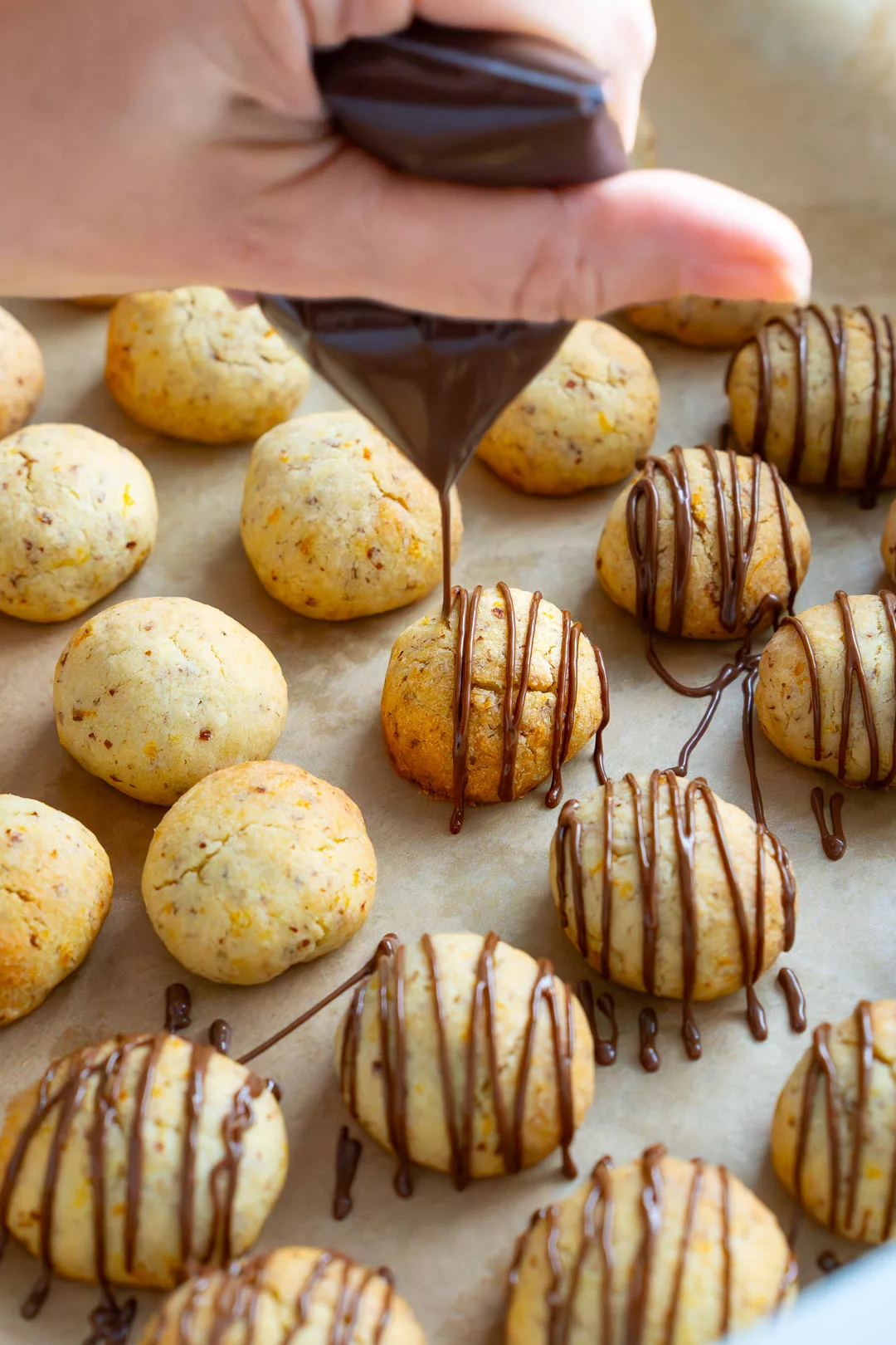 Nahaufnahme: Eine Hand verzierte die Orangen-Wölkchen Plätzchen mit flüssiger Zartbitterschokolade aus einem Spritzbeutel.