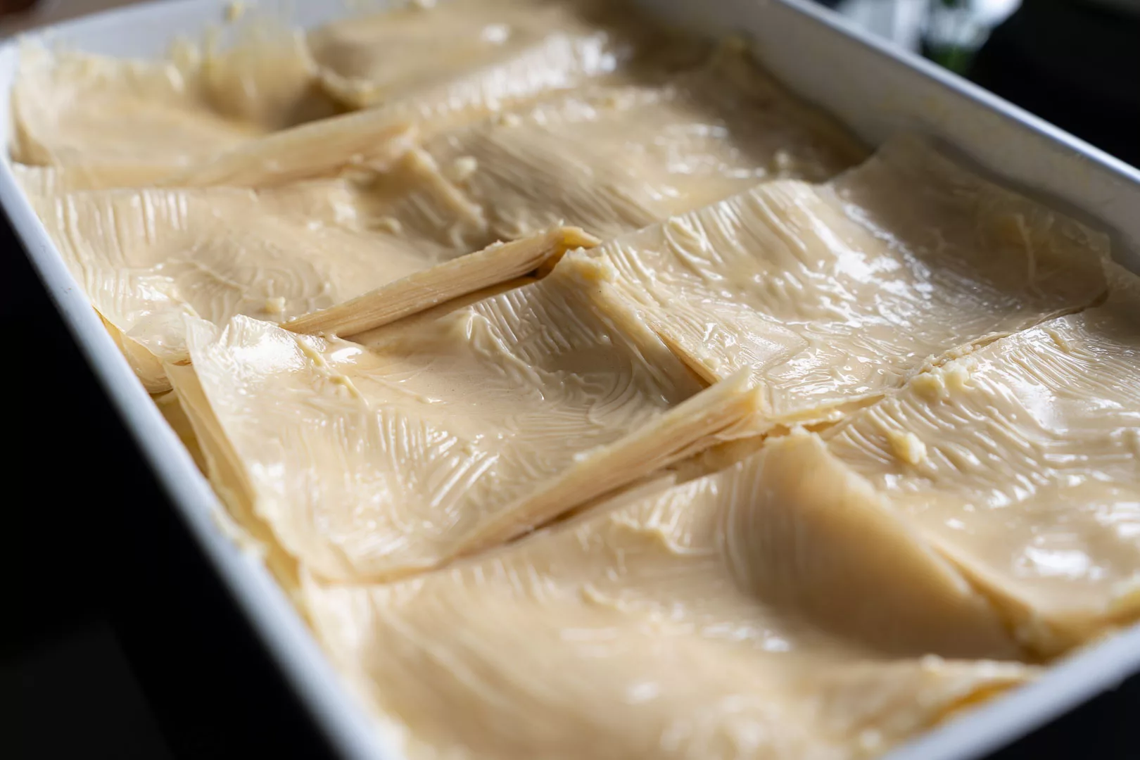 Eine Auflaufform mit ungebackenem Galaktoboureko, gefüllt mit cremiger Grießmasse und bedeckt mit mehreren Schichten rohem Filoteig, bereit zum Backen.