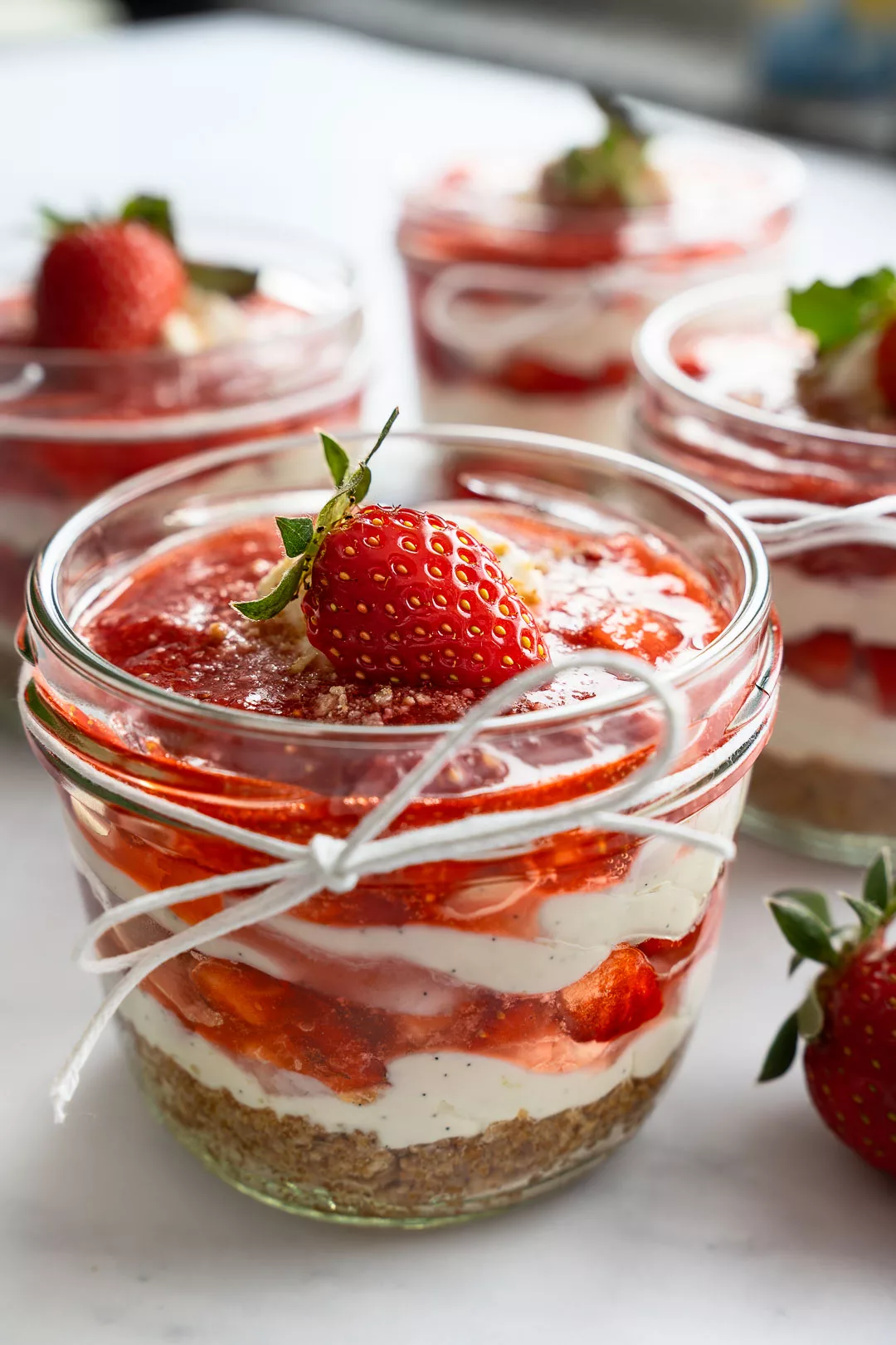 Erdbeer-Tiramisu im Glas mit Keksboden, cremiger Mascarpone-Quark-Schicht, fruchtigem Erdbeer-Topping und frischer Erdbeere als Dekoration.