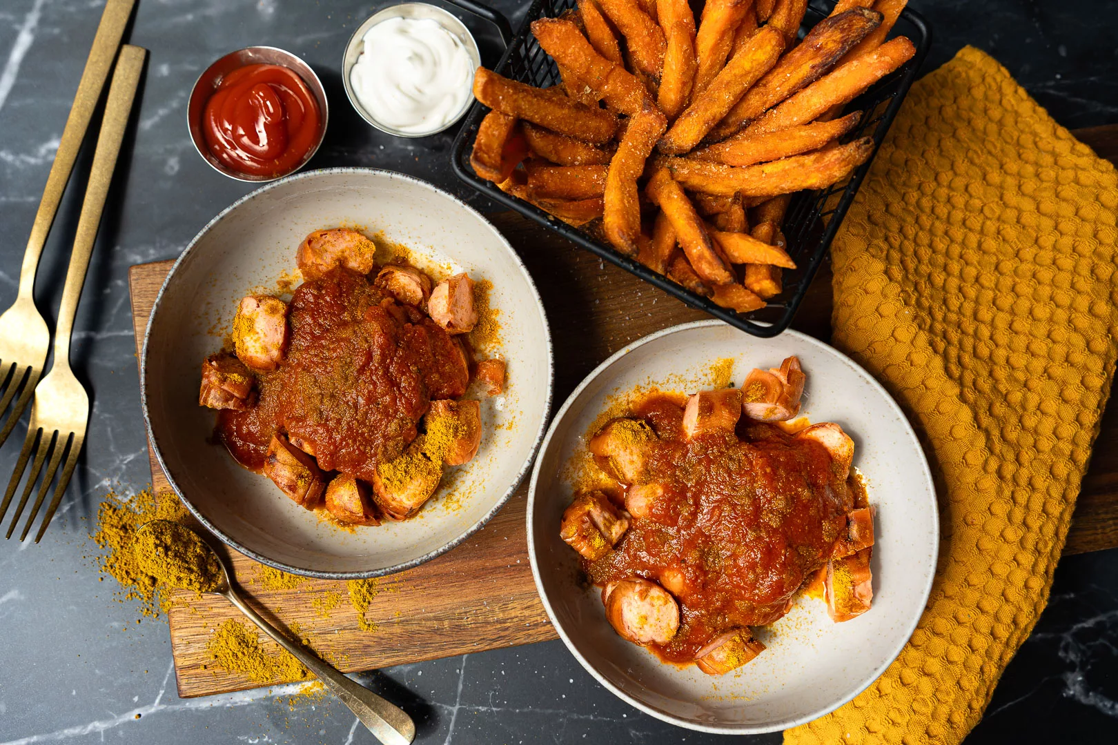 Selbstgemachte Currywurst mit roter Currysoße, Currypulver und Pommes auf einem Teller als klassisches Imbissgericht.