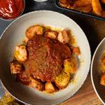 Currywurst mit würziger roter Currysoße, Currypulver und Pommes auf einem Teller als selbstgemachter Imbiss-Klassiker.