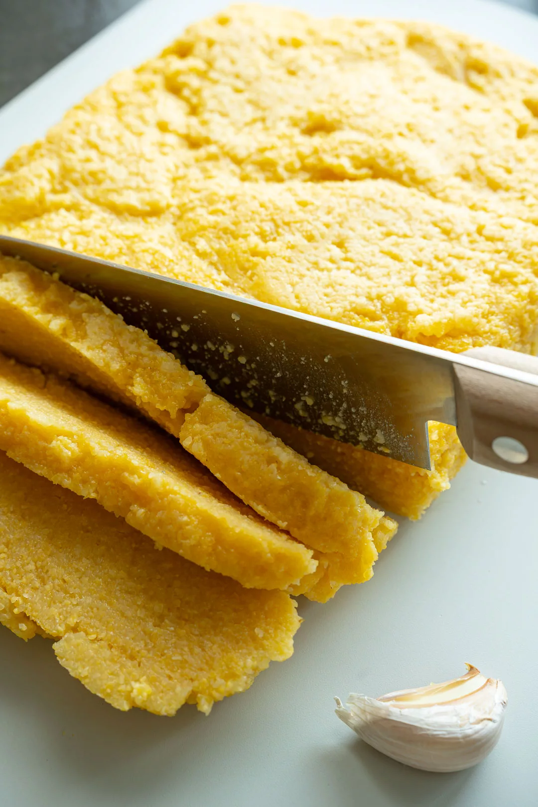 Ausgekühlte Polenta wird mit einem großen Messer auf einem Schneidebrett in gleichmäßige Scheiben geschnitten.