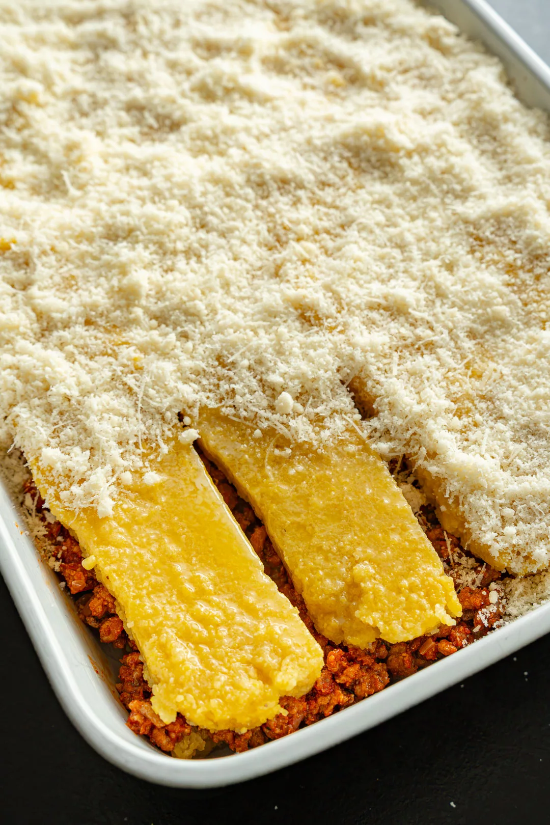 Auflaufform mit würzigem Ragù, darauf geschichteten Polentascheiben und einer großzügigen Schicht geriebenem Käse.