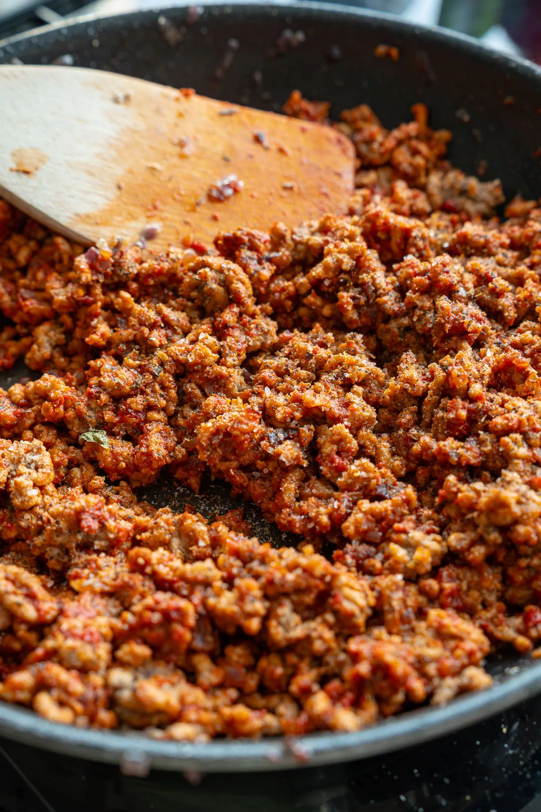 Würziges Hackfleisch-Ragù mit Tomatensauce und Kräutern in einer schwarzen Pfanne, daneben ein großer Holzlöffel.