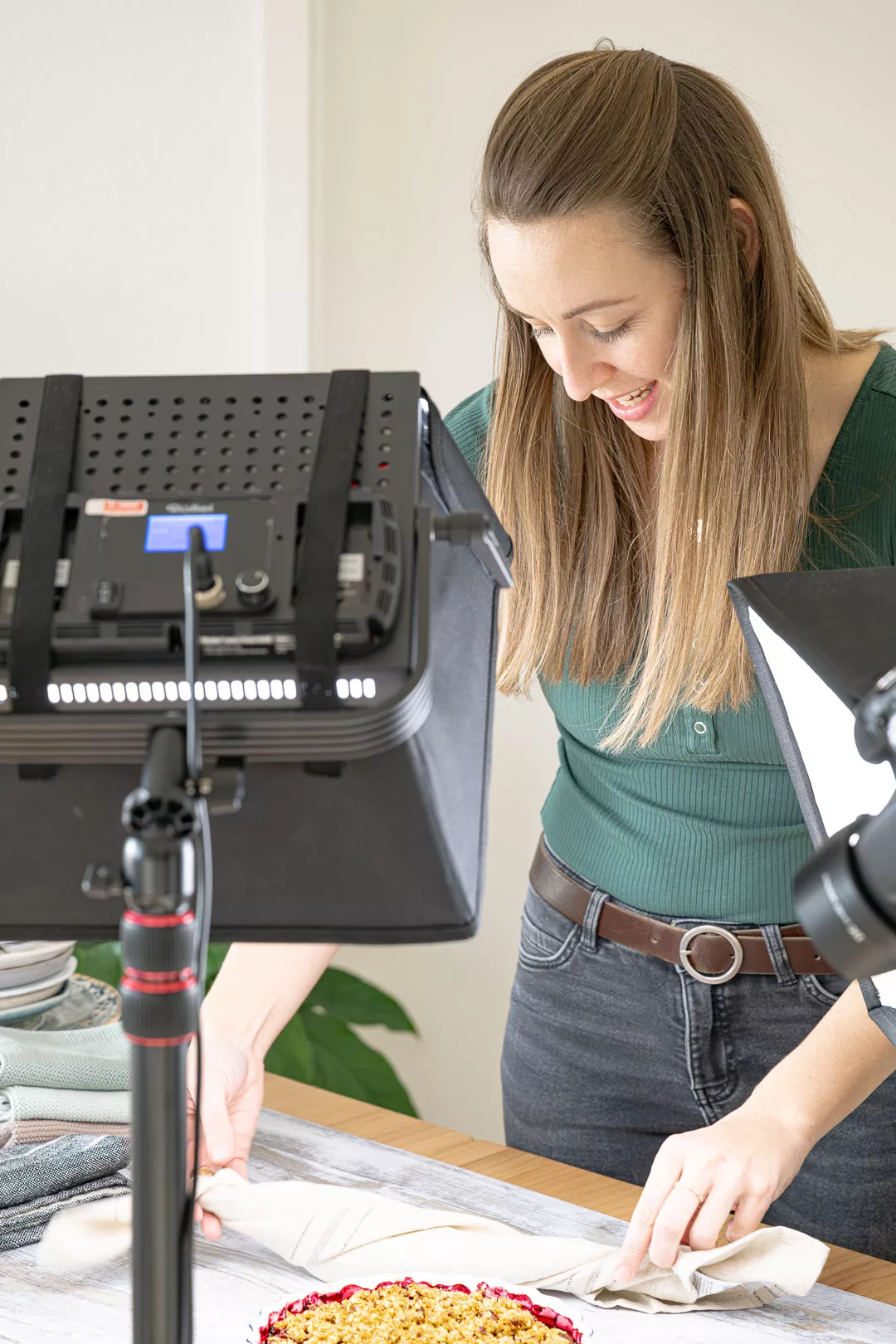 Adele beim Arrangieren eines Gerichts auf einem Fotohintergrund, umgeben von Kamera und Studiolichtern für ein professionelles Food-Fotoshooting.