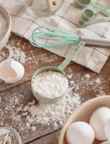 Mengen umrechnen beim Backen: Backzutaten wie Mehl in Schalen, Eier und Zucker auf einer Arbeitsfläche in der Küche.
