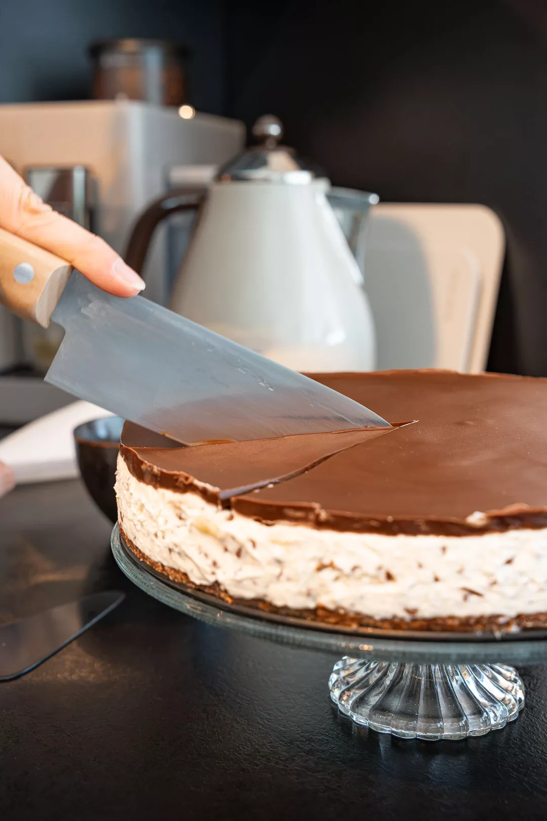 Bananensplit Torte auf Kuchenplatte mit Bananenscheiben, Sahnehauben und Schokoladensauce auf rustikalem Holztisch.