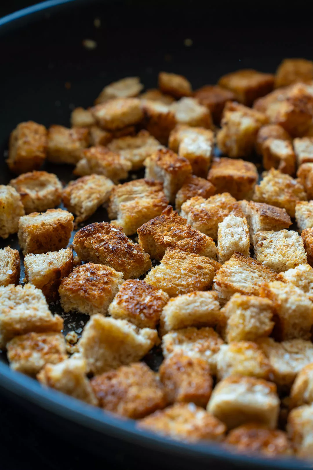 Goldbraun geröstete Brotwürfel werden in einer schwarzen Pfanne zu knusprigen Croutons gebraten.
