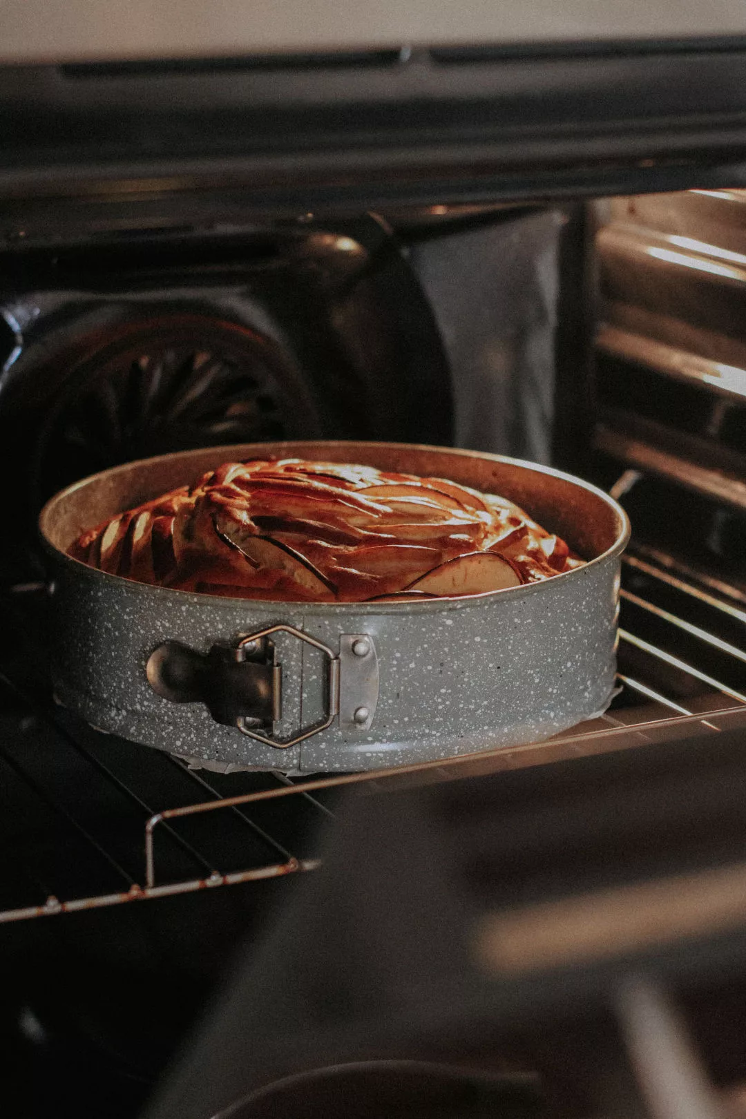 Goldbraun gebackener Kuchen in einer runden Springform auf dem Rost im beleuchteten Backofen.