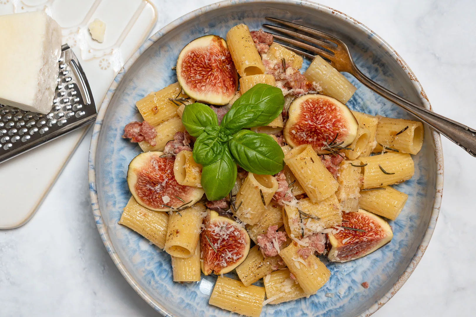 Teller mit Pasta, gebratenen Salsiccia-Stücken, frischen Feigenvierteln und Kräutern garniert.