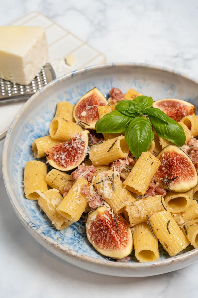 Pasta mit frischen Feigen und gebratener Salsiccia serviert auf einem Teller.