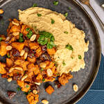 Geröstete Saté Süßkartoffeln angerichtet auf Hummus mit Erdnusssauce und Kräutern in Schale.