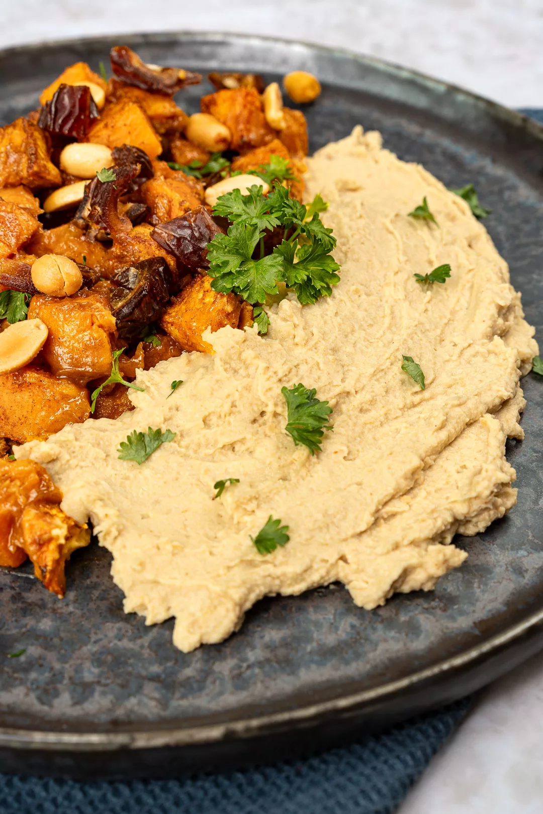 Saté Süßkartoffeln auf cremigem Hummus mit Erdnusssoße und frischem Koriander in flacher Schale serviert.