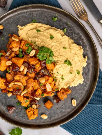 Geröstete Saté Süßkartoffeln angerichtet auf Hummus mit Erdnusssauce und Kräutern in Schale.