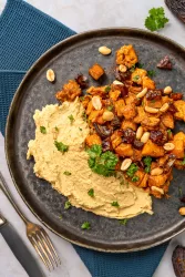 Geröstete Saté Süßkartoffeln angerichtet auf Hummus mit Erdnusssauce und Kräutern in Schale.