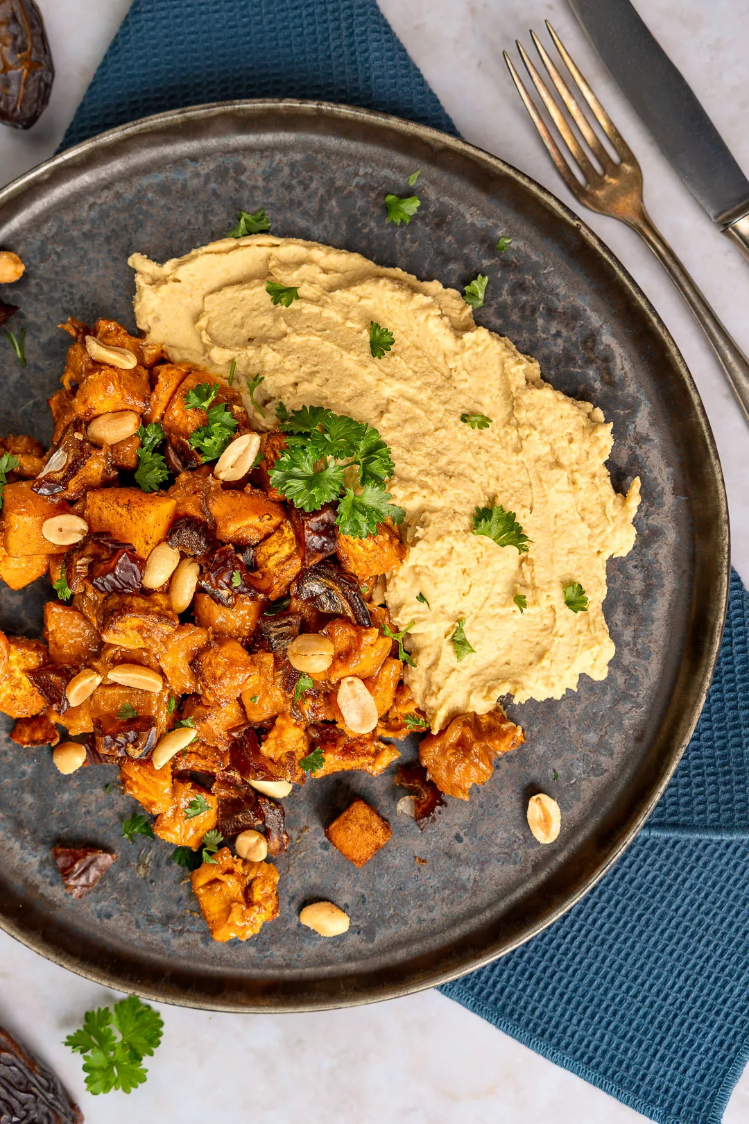 Geröstete Saté Süßkartoffeln angerichtet auf Hummus mit Erdnusssauce und Kräutern in Schale.