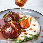 Gebackene Feigen mit Mascarpone auf einem rustikalen Teller, beträufelt mit Honig und gehackten Nüssen.