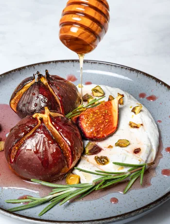 Gebackene Feigen mit Mascarpone auf einem rustikalen Teller, beträufelt mit Honig und gehackten Nüssen.