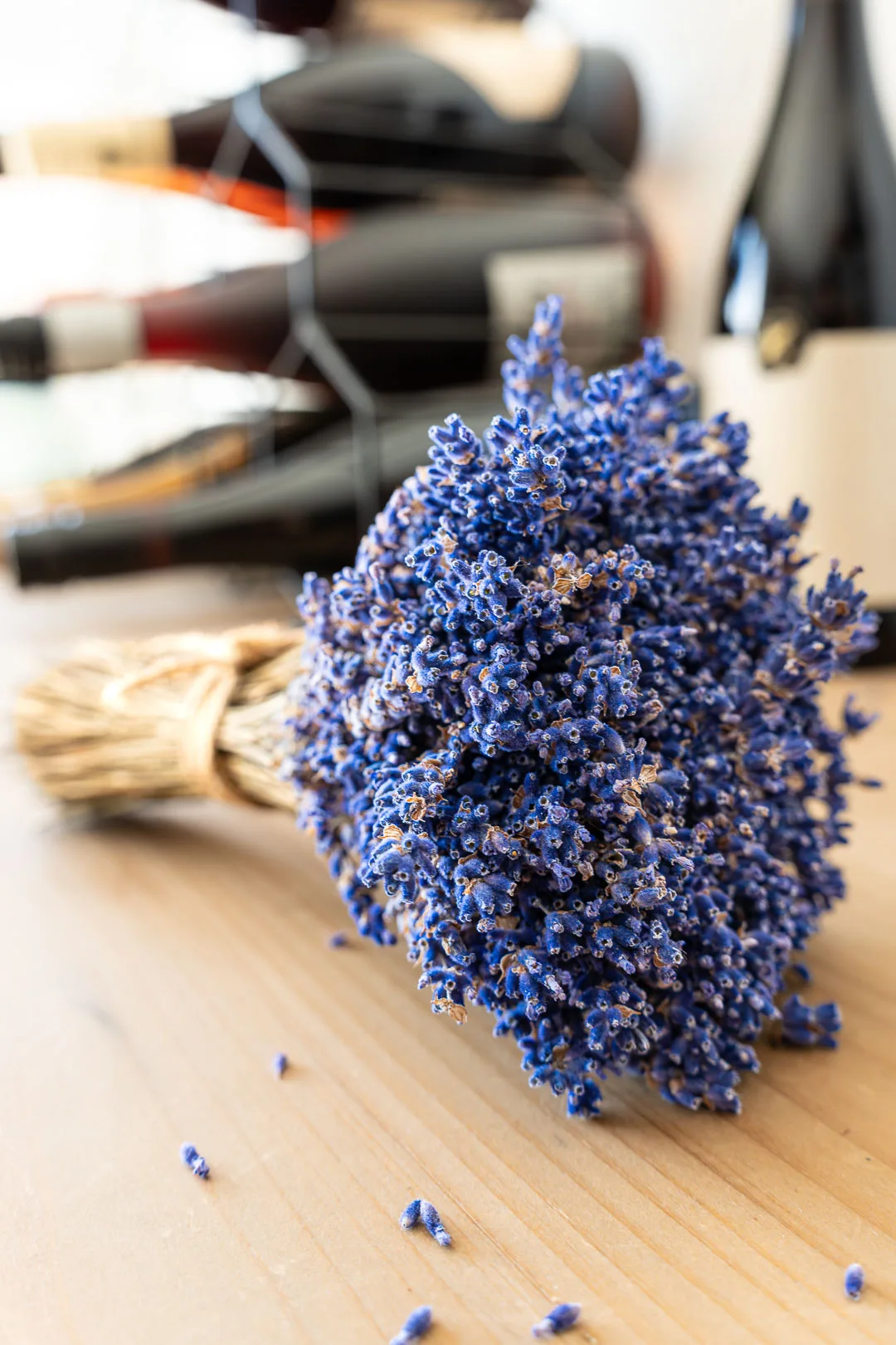 Yummy Lavender: Getrockneter, gebundener Lavendelstrauß auf Holztisch, lose Blüten, Weinregal im Hintergrund.