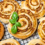 Pizzaschnecken mit Pesto auf einem schwarzen Kuchengitter, garniert mit frischem Basilikum.
