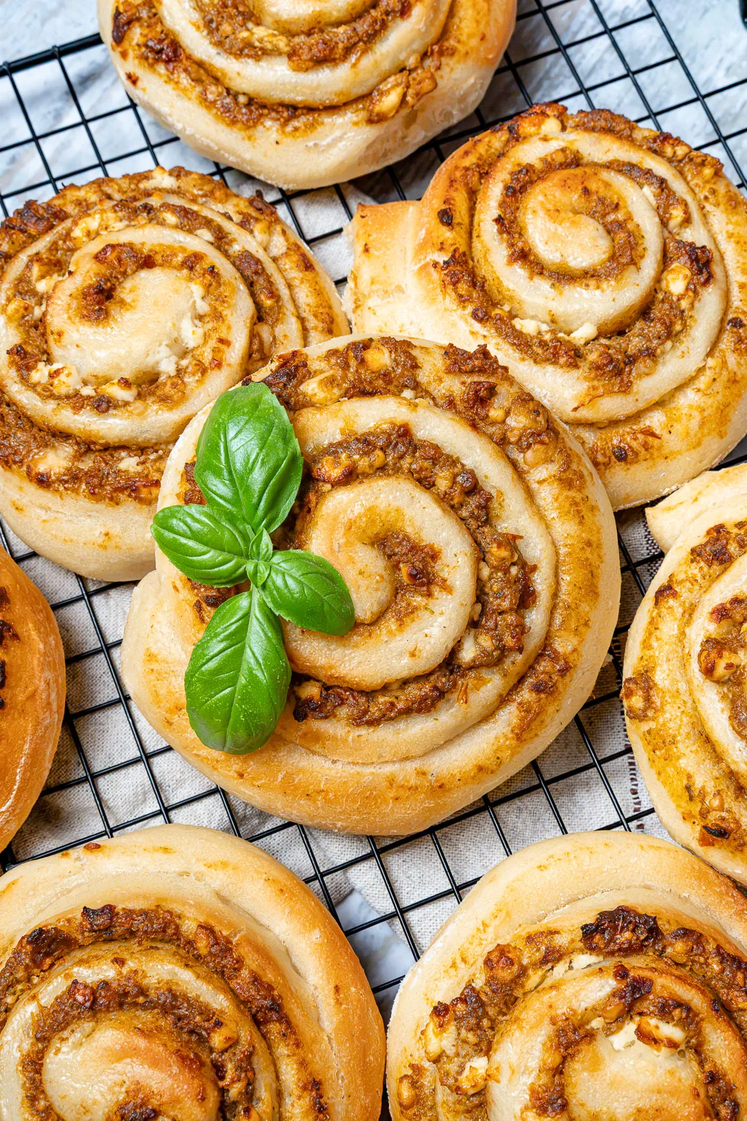 Pizzaschnecken mit Pesto auf einem schwarzen Kuchengitter, garniert mit frischem Basilikum.