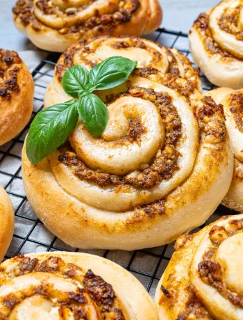 Pizzaschnecken mit Pesto auf einem Kuchengitter, garniert mit frischen Basilikumblättern.