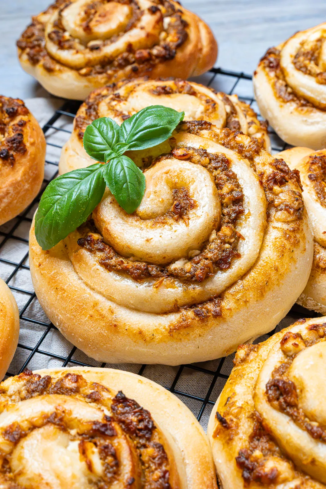 Pizzaschnecken mit Pesto auf einem Kuchengitter, garniert mit frischen Basilikumblättern.