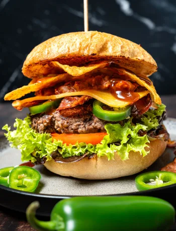 Tex Mex Burger mit Bohnen Mash auf dunklem Teller, mit Fleisch-Patty, geschmolzenem Cheddar und Zwiebelringen.