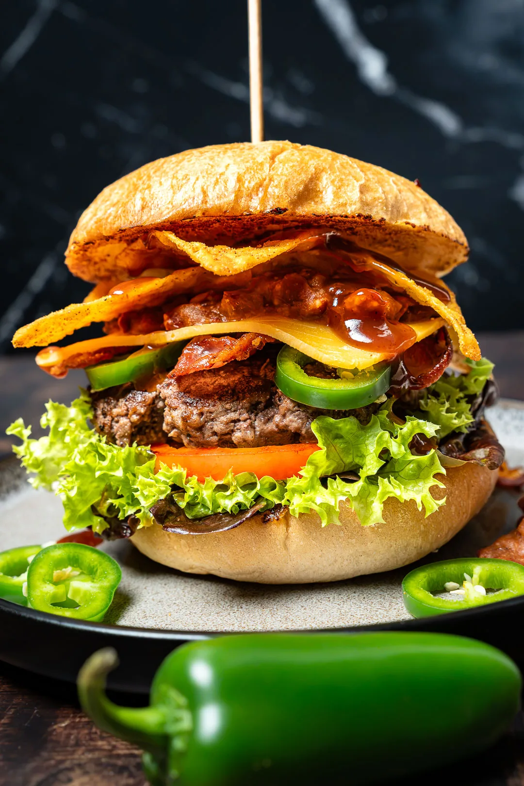 Tex Mex Burger mit Bohnen Mash auf dunklem Teller, mit Fleisch-Patty, geschmolzenem Cheddar und Zwiebelringen.