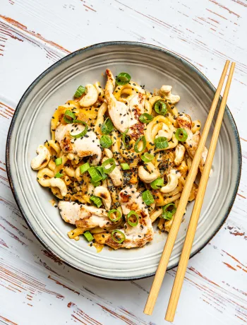 Udon-Nudeln mit Hoisin-Huhn und glänzender Sauce in einer Schale, garniert mit Sesam und Frühlingszwiebeln.