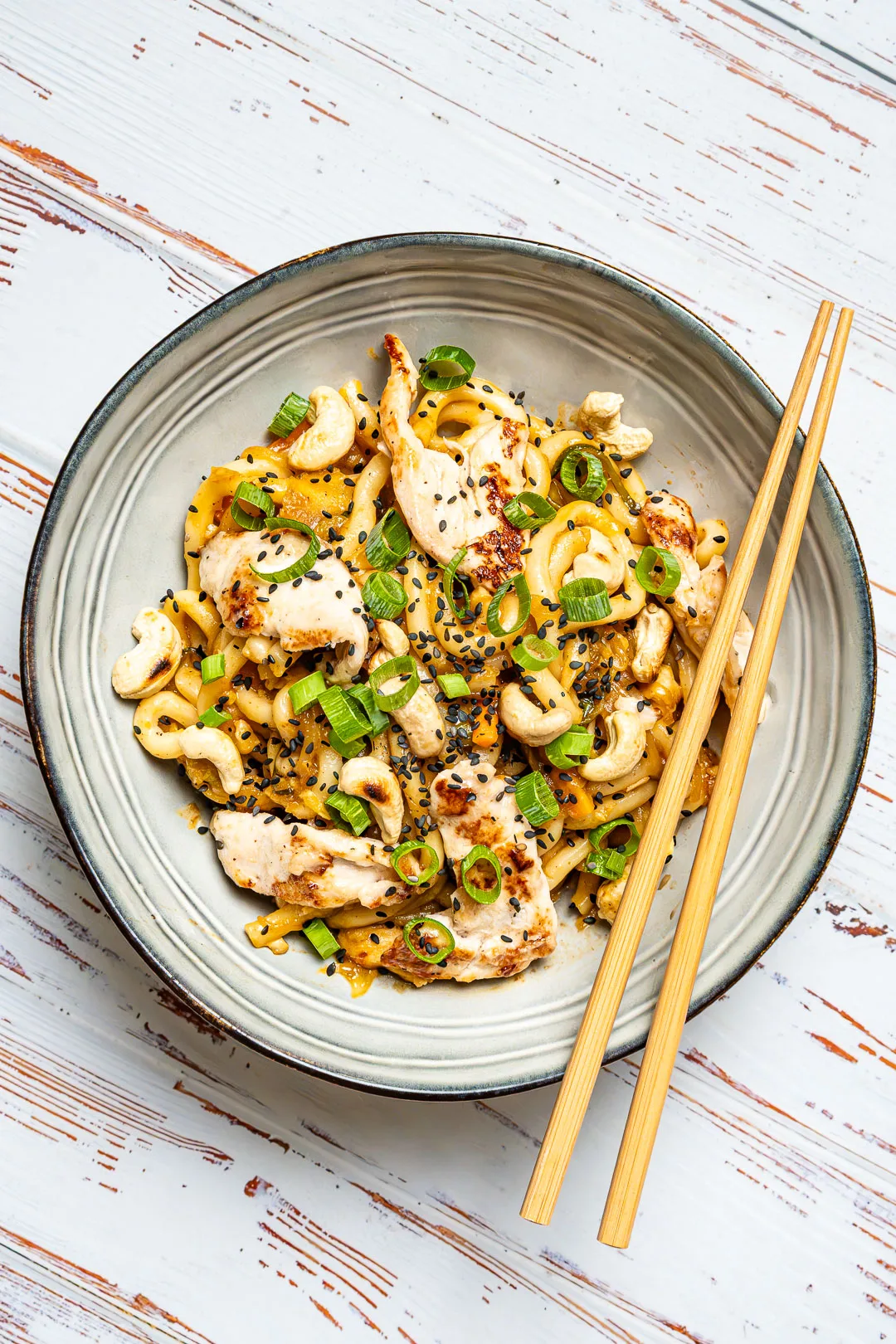 Udon-Nudeln mit Hoisin-Huhn und glänzender Sauce in einer Schale, garniert mit Sesam und Frühlingszwiebeln.