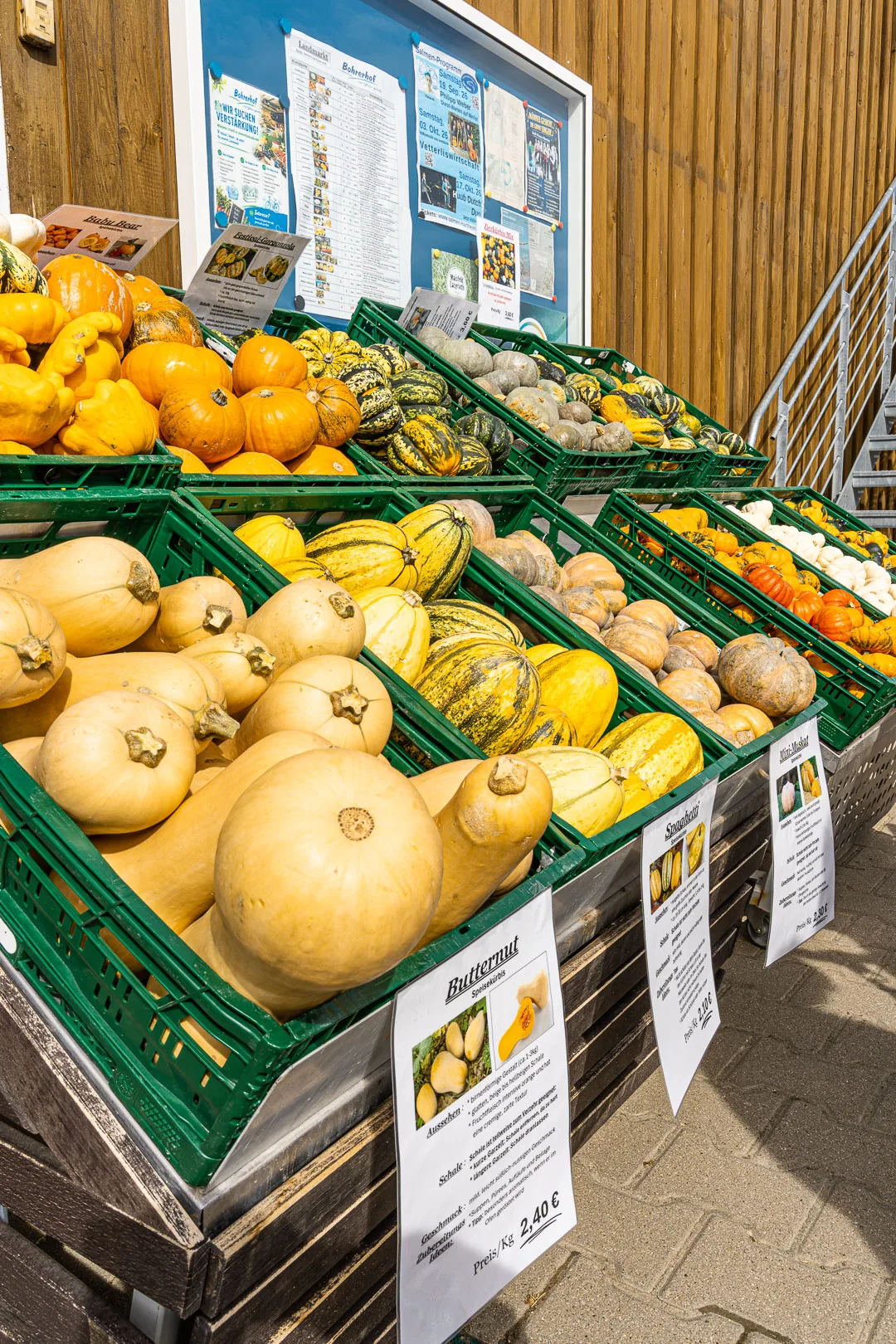 Marktstand mit Kürbissen für leckere Herbstrezepte: Verschiedene rohe Kürbisse in grünen Kisten an einem Verkaufsstand mit Schildern.